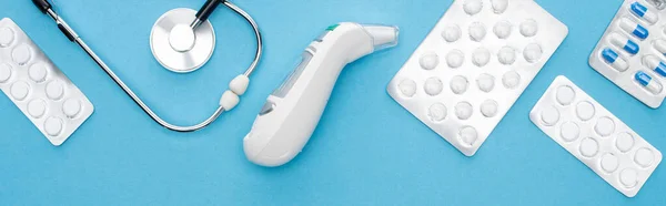 Top view of pills in blister packs, stethoscope and ear thermometer on blue background, horizontal image — Stock Photo