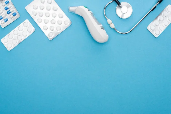 Ansicht von Pillen in Blisterverpackungen, Stethoskop und Ohrthermometer auf blauem Hintergrund, horizontales Bild — Stockfoto