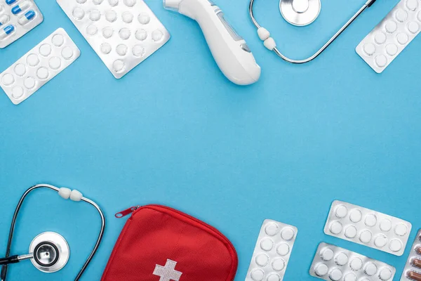 Vista dall'alto di pillole in blister, stetoscopi, kit di pronto soccorso e termometro auricolare su sfondo blu — Foto stock