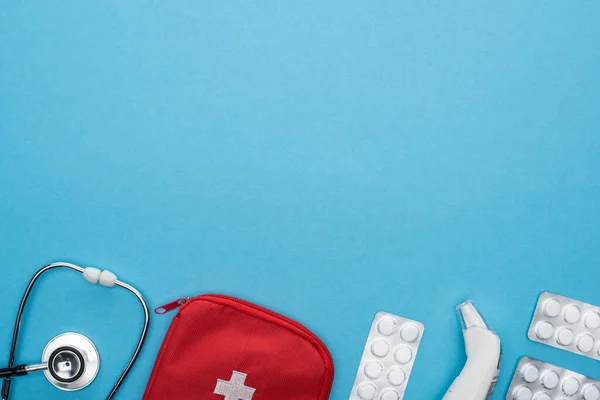 Вид зверху таблеток у блістерних упаковках, стетоскоп, аптечка для першої допомоги та вушний термометр на синьому фоні — стокове фото