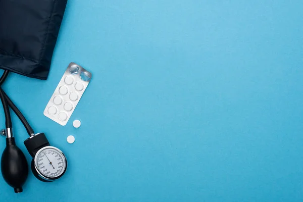 Vue du dessus des pilules en plaquette thermoformée, sphygmomanomètre sur fond bleu — Photo de stock