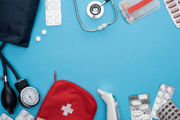 Ansicht von Ohrenthermometer, Pillen in Blisterverpackungen, Blutdruckmessgerät, Verbandskasten und Stethoskop auf blauem Hintergrund — Stockfoto