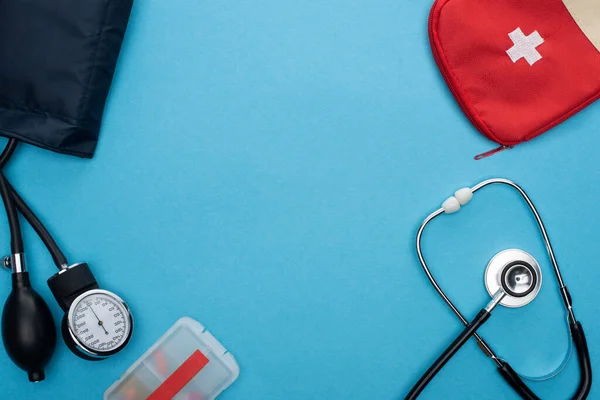 Vue du dessus des pilules en récipient, sphygmomanomètre, trousse de premiers soins et stéthoscope sur fond bleu — Photo de stock