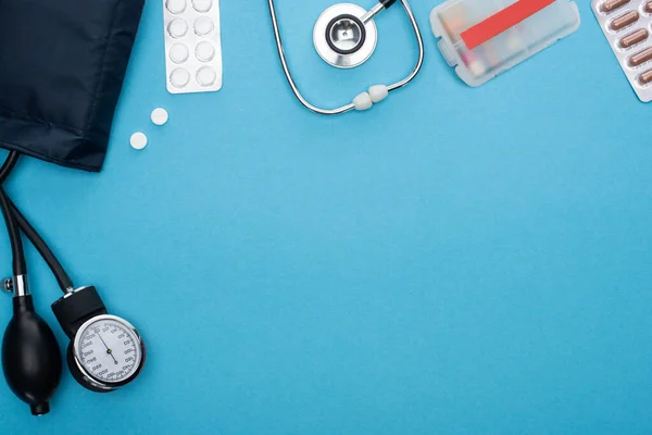 Вид зверху таблеток у блістерних пачках, сфінгометрі та стетоскопі на синьому фоні — стокове фото