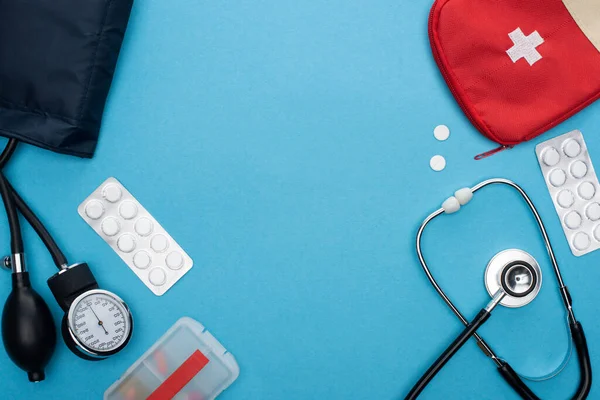 Vue du dessus des pilules en plaquettes thermoformées, sphygmomanomètre, trousse de premiers soins et stéthoscope sur fond bleu — Photo de stock