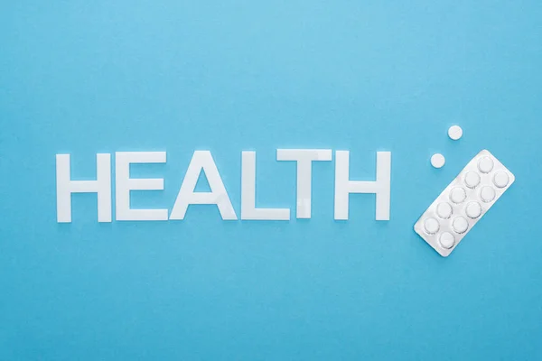 Top view of pills in blister pack and health lettering on blue background — Stock Photo