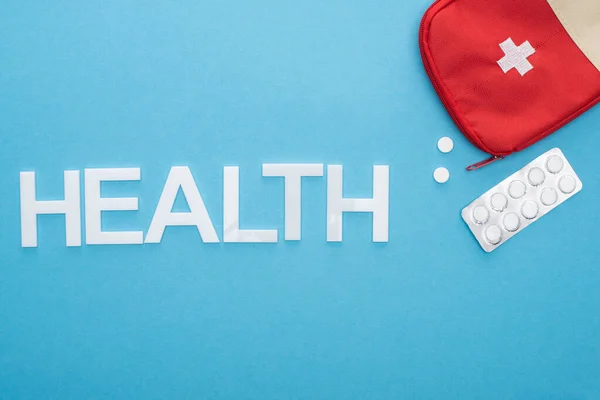 Top view of pills in blister pack, first aid kit and health lettering on blue background — Stock Photo