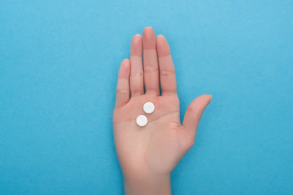 Частичный вид женщины, держащей таблетки на синем фоне — стоковое фото