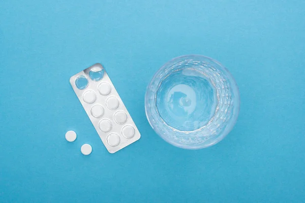 Top view of pills in blister pack, glass of water on blue background — Stock Photo