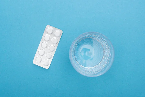Top view of pills in blister pack, glass of water on blue background — Stock Photo
