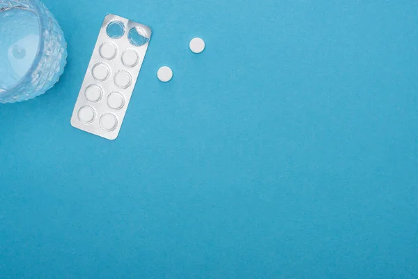 Top view of pills in blister pack, glass of water on blue background — Stock Photo