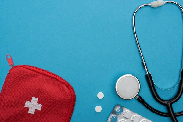 Ansicht von Pillen in Blisterverpackung, Stethoskop, Verbandskasten auf blauem Hintergrund — Stockfoto