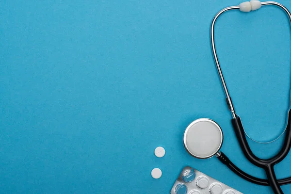 Top view of pills in blister pack, stethoscope on blue background — Stock Photo