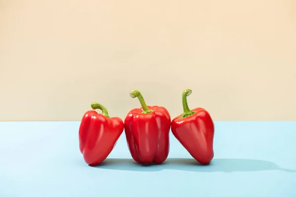 Fresh red bell peppers on blue surface isolated on beige — Stock Photo