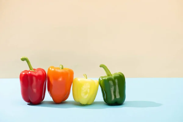 Fresh colorful bell peppers on blue surface isolated on beige — Stock Photo