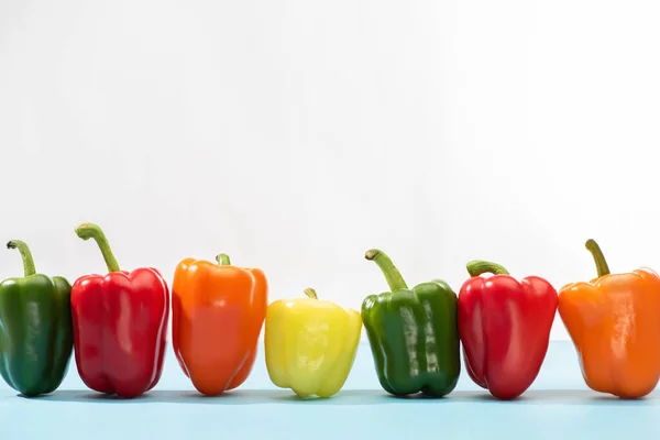 Poivrons colorés frais sur la surface bleue sur fond blanc — Photo de stock