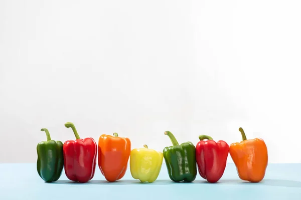 Fresh colorful bell peppers in row on blue surface on white background — Stock Photo