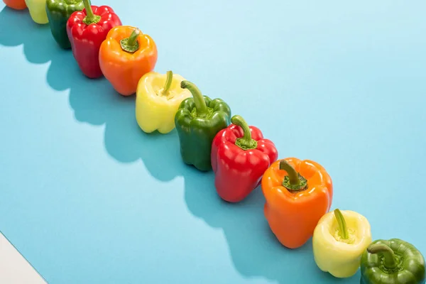 Fresh colorful bell peppers in row on blue surface — Stock Photo