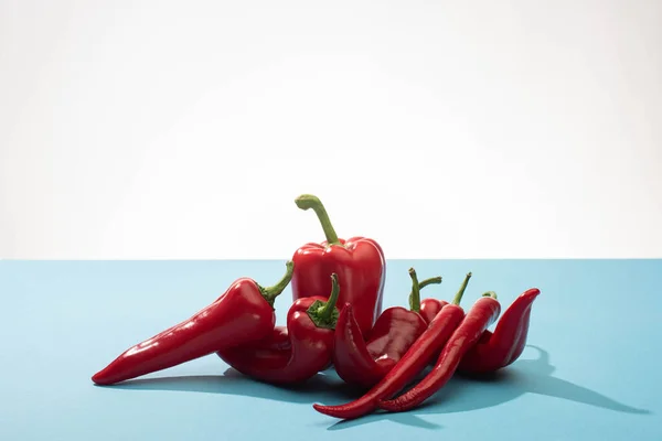 Fresh red bell peppers and chili on blue surface on white background — Stock Photo