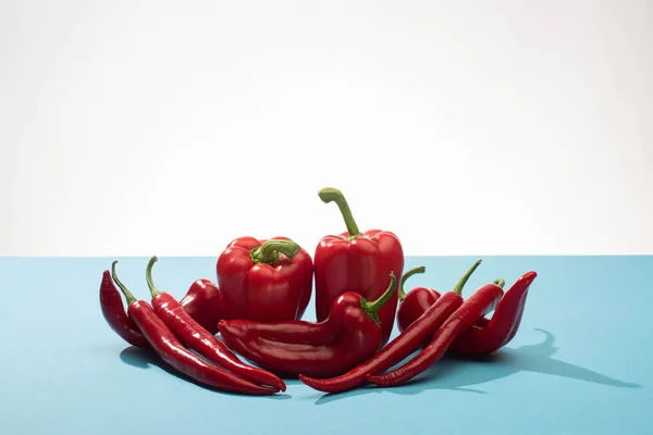 Fresh red bell peppers and chili on blue surface on white background — Stock Photo