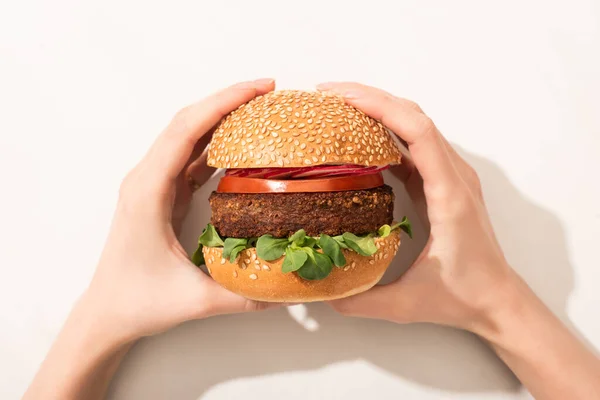 Vista recortada de la mujer sosteniendo deliciosa hamburguesa vegana con rábano sobre fondo blanco - foto de stock