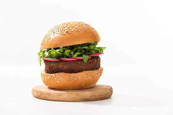 Вкусный веганский бургер с редькой и рукколой на деревянной доске на белом фоне — стоковое фото