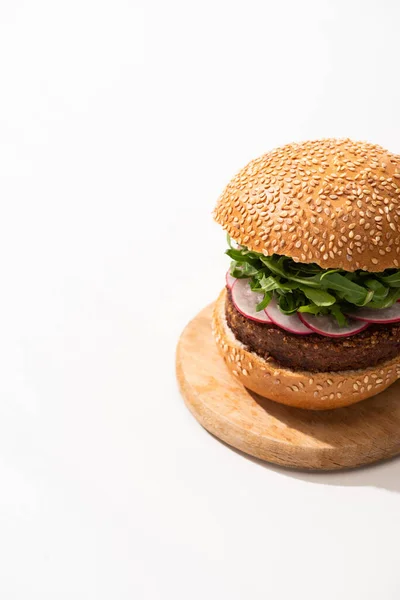 Deliciosa hamburguesa vegana con rábano y rúcula sobre tabla de madera sobre fondo blanco - foto de stock