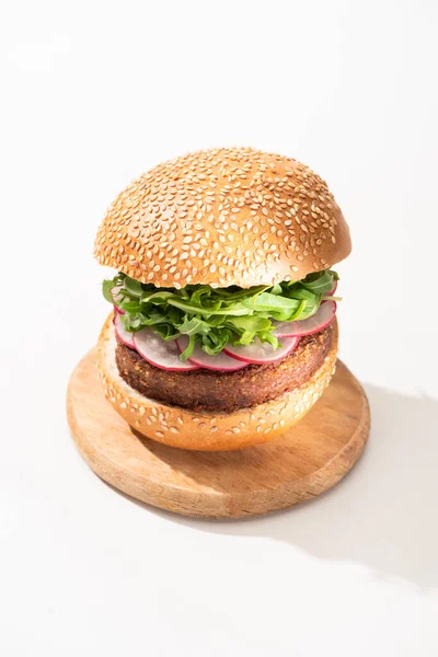 Deliciosa hamburguesa vegana con rábano y rúcula sobre tabla de madera sobre fondo blanco - foto de stock
