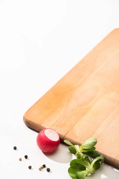 Rabanete delicioso e verdes com pimenta preta perto de tábua de madeira no fundo branco — Fotografia de Stock