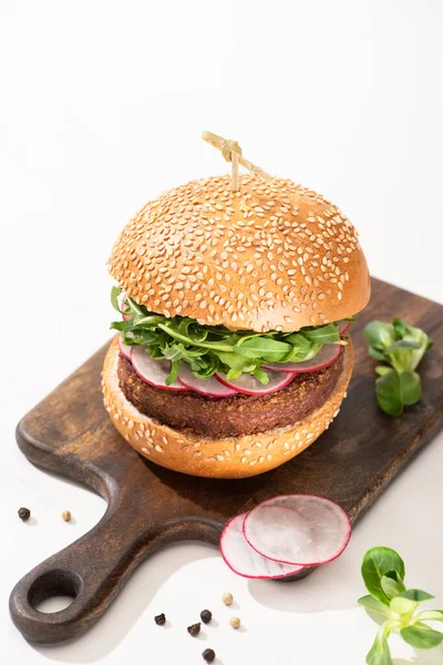 Delicioso hambúrguer vegan com rabanete e rúcula na placa de madeira com pimenta preta no fundo branco — Fotografia de Stock