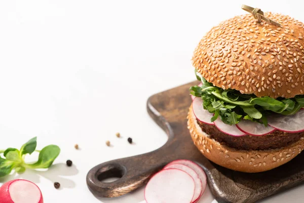 Selective focus of  delicious vegan burger with radish and arugula on wooden board with black pepper on white background — Stock Photo