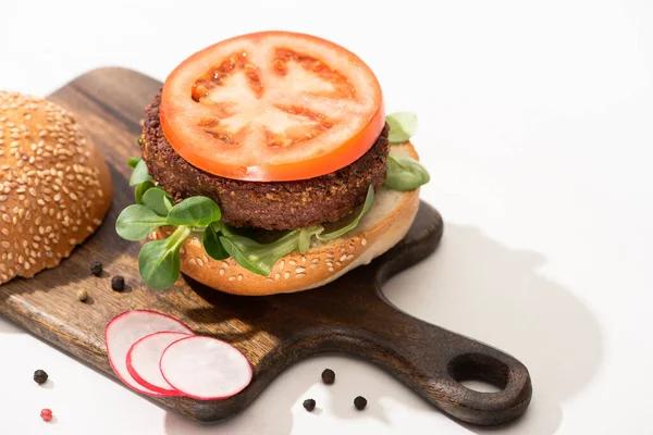 Delicious vegan burger with radish, tomato and microgreens on wooden boar with black pepper on white background — Stock Photo