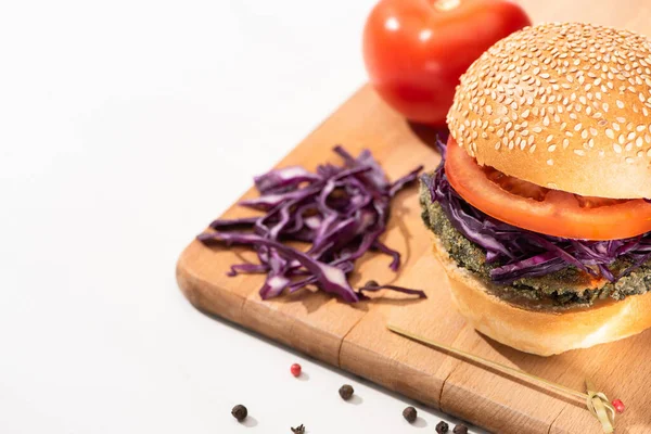 Вкусный веганский бургер с красной капустой и помидорами на деревянной доске с черным перцем на белом фоне — стоковое фото