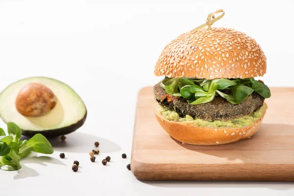 Deliciosa hamburguesa verde vegana con microgreens, aguacate, pimienta negra sobre tabla de madera sobre fondo blanco - foto de stock