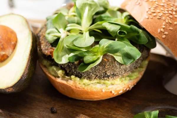 Vista da vicino di delizioso hamburger vegan verde con microverdi, avocado sul tagliere di legno — Foto stock