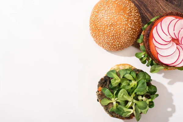 Vista superior de hamburguesas veganas con microgreens, rábano sobre tabla de cortar sobre fondo blanco - foto de stock