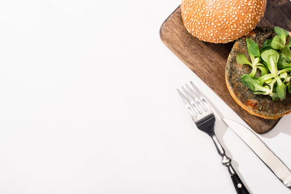 Top view of vegan burger with microgreens on wooden board near cutlery on white background — Stock Photo