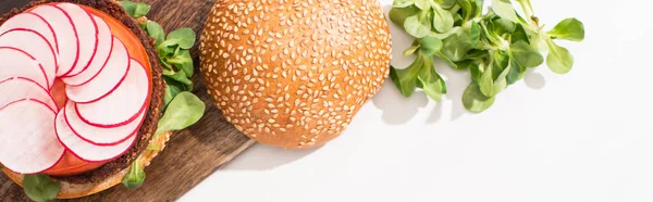 Вид сверху на веганский бургер с микрозеленью, редис на деревянной доске резки на белом фоне, панорамный снимок — Stock Photo