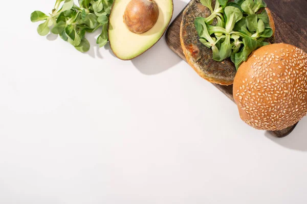 Вид на веганский бургер с микрозеленью и авокадо на деревянной доске для резки на белом фоне — стоковое фото