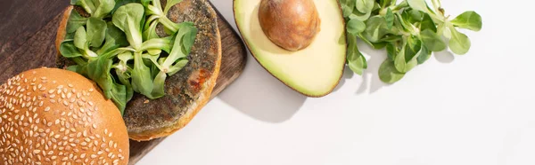 Top view of vegan burger with microgreens and avocado on wooden cutting board on white background, panoramic shot — Stock Photo