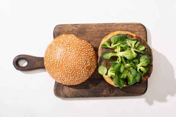 Vista superior de hamburguesa vegana con microgreens en tabla de cortar de madera sobre fondo blanco - foto de stock