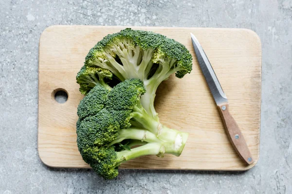 Top view of fresh green cut broccoli on wooden cutting board with knife on grey surface — Stock Photo