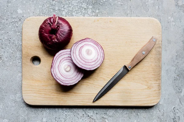 Top view of onion on wooden cutting board with knife on grey concrete surface — Stock Photo