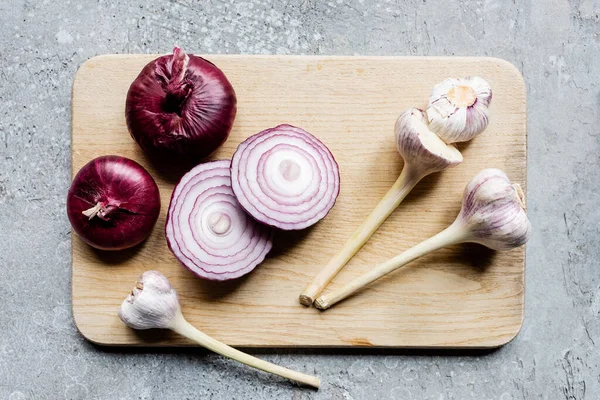Top view of onion and garlic on wooden cutting board on grey concrete surface — Stock Photo