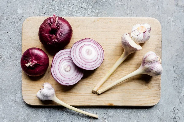 Ansicht von Zwiebel und Knoblauch auf Holzschneidebrett auf grauer Betonoberfläche — Stockfoto