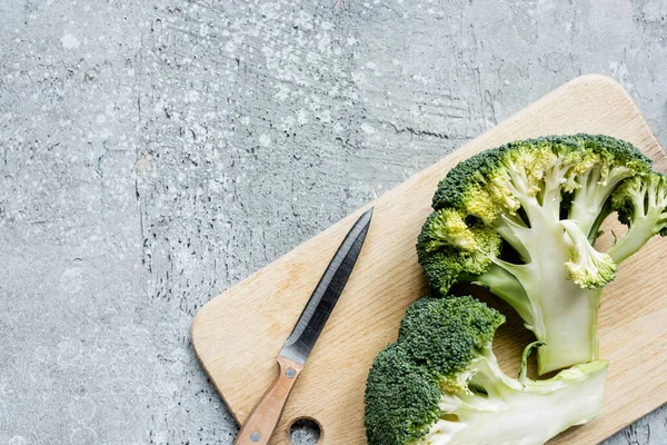 Top view of fresh green cut broccoli on wooden cutting board with knife on grey surface — Stock Photo