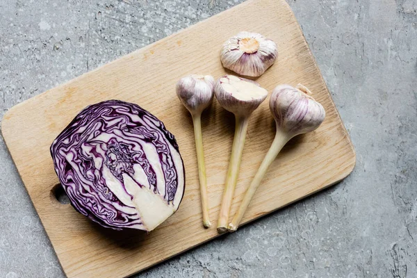 Top view of red cabbage and garlic on wooden cutting board on grey concrete surface — Stock Photo