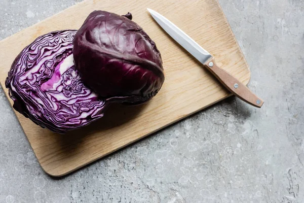 Top view of red cabbage on wooden cutting board with knife on grey concrete surface — Stock Photo