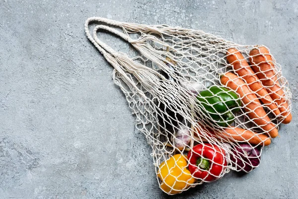 Top view of fresh ripe vegetables in string bag on grey concrete surface — Stock Photo