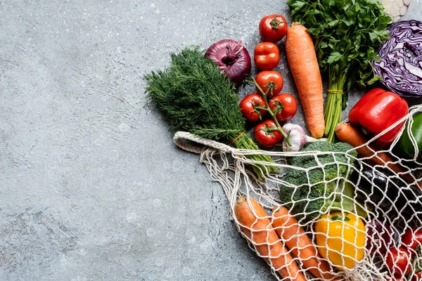 Top view of fresh ripe vegetables in string bag on grey concrete surface — Stock Photo